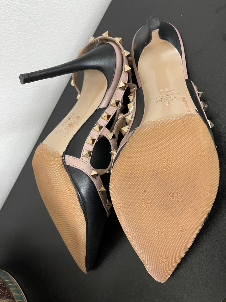 May include: Black and pink leather high heel shoes with gold studs and a Valentino logo on the sole.