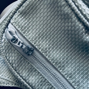 K&ouml;nnte beinhalten: Nahaufnahme eines grauen Rei&szlig;verschlusses auf einer strukturierten Stofftasche.