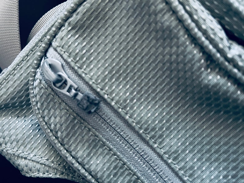 K&ouml;nnte beinhalten: Nahaufnahme eines grauen Rei&szlig;verschlusses auf einer strukturierten Stofftasche.