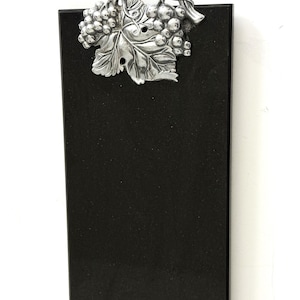May include: A rectangular black serving board with a silver-colored grape and leaf design at the top. The decorative element features detailed grapes and a large leaf, adding a touch of elegance to the serving piece.