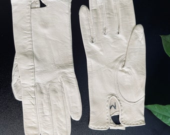 May include: A pair of white leather gloves with a small 'M' stitched on the wrist of one glove.