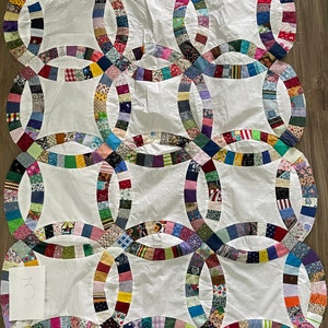 May include: A white quilt with a double wedding ring pattern. The quilt is made of many different fabrics in various colors and patterns. The quilt is hand-stitched and has a handwritten number "33" on a piece of paper in the lower left corner.