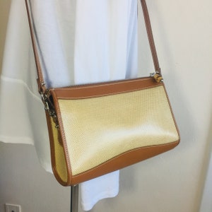 May include: A tan and brown woven crossbody bag with a leather trim and a zipper closure.