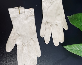 May include: A pair of off-white leather gloves with a stitched detail around the wrist and a gold button closure.