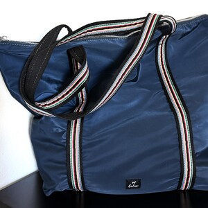 May include: A navy blue tote bag with black handles and a zipper closure. The bag features a striped accent in red, white, and green. The bag has a small black label with the word "Echo" on it.