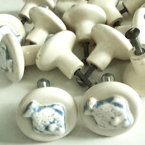 May include: A collection of off-white ceramic cabinet knobs with a blue and white sheep design. The knobs have a rounded shape and are attached to metal screws. Ideal for adding a rustic touch to furniture.