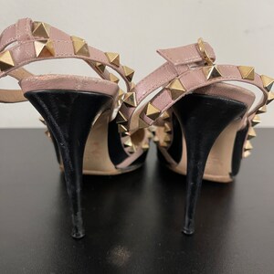 May include: A pair of black and blush pink high heel shoes with gold pyramid studs. The shoes have a pointed toe and an ankle strap.