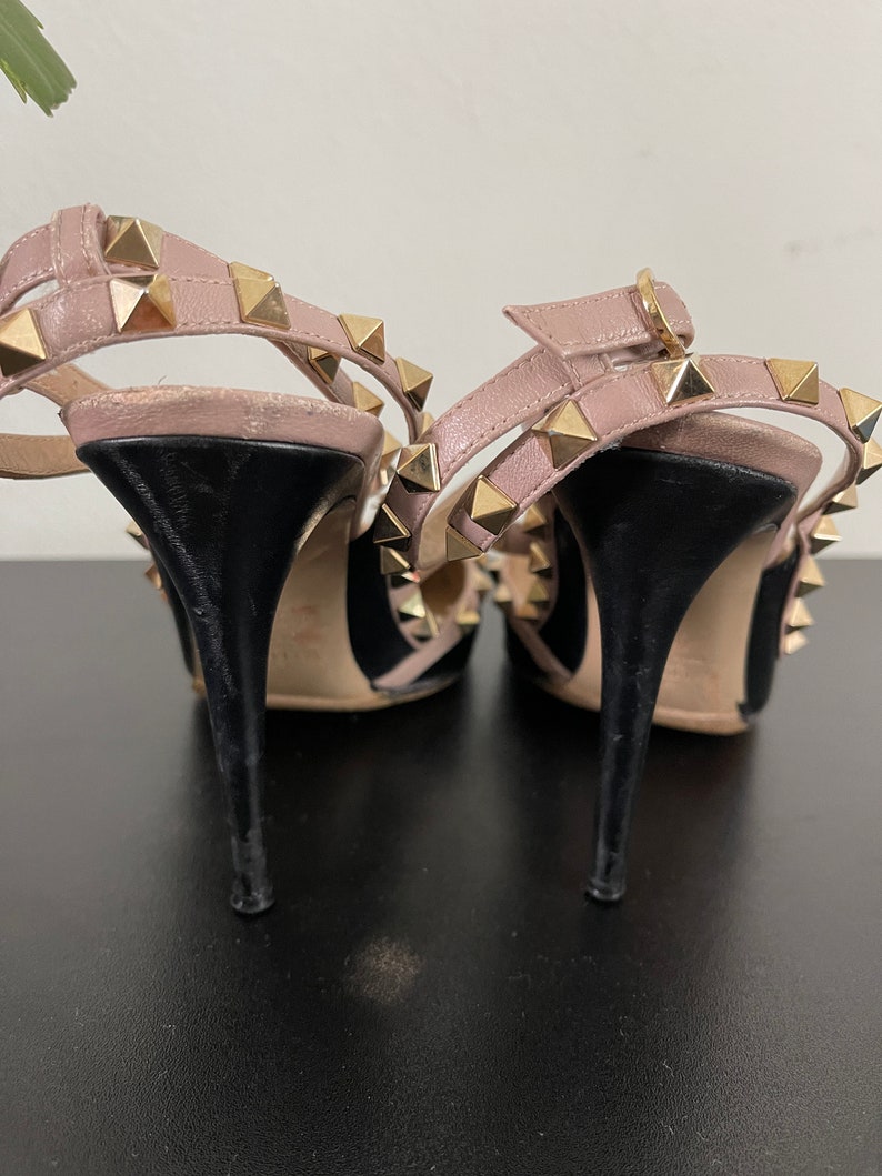 May include: A pair of black and blush pink high heel shoes with gold pyramid studs. The shoes have a pointed toe and an ankle strap.
