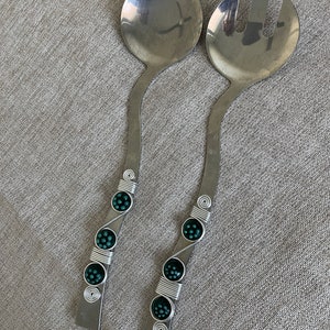 May include: A set of two silver salad serving utensils with green beaded accents. The utensils have a curved handle and are made of stainless steel.