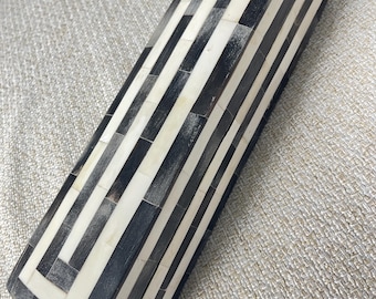 May include: A black and white striped box made of bone. The box has a geometric pattern and is rectangular in shape.