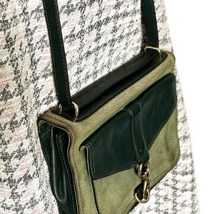 May include: A crossbody bag featuring a two-tone design with dark forest green leather accents and a lighter sage green textured leather body. The bag includes a dark green shoulder strap, a front flap pocket, and a gold-toned metal swivel clasp.