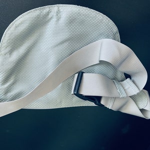 K&ouml;nnte beinhalten: Eine hellgraue Stoff-Bauchtasche mit einem verstellbaren wei&szlig;en Gurt und einer schwarzen Schnalle.