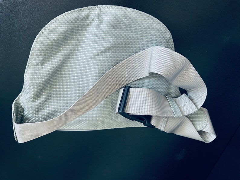 K&ouml;nnte beinhalten: Eine hellgraue Stoff-Bauchtasche mit einem verstellbaren wei&szlig;en Gurt und einer schwarzen Schnalle.