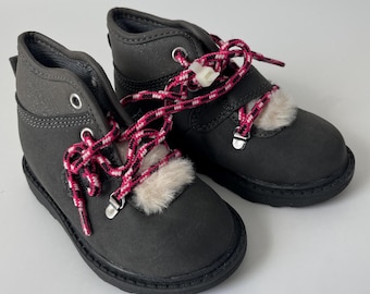 May include: A pair of black suede boots with pink and white laces. The boots have a faux fur trim around the ankle.