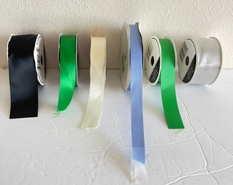 May include: Assortment of six spools of ribbon in various colors, including black, green, white, and blue. The ribbon is wound around cardboard spools with labels.