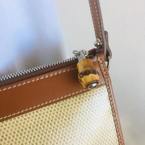 May include: A brown and beige woven shoulder bag with a brown leather trim and a bamboo-style zipper pull.