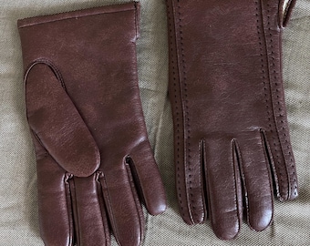 May include: A pair of brown leather gloves with stitching detail. The gloves have a long cuff and are made of a soft, supple leather.