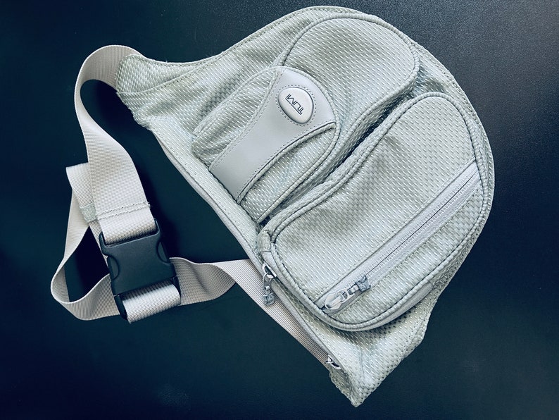 May include: A gray mesh sling bag with a zippered pocket and a black buckle strap. The bag has a white logo that says "ECCO" on the front.