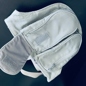 K&ouml;nnte beinhalten: Eine graue Mesh-Bauchtasche mit zwei Rei&szlig;verschlussf&auml;chern und einer Klettverschlusslasche. Die Tasche hat einen Trageriemen.