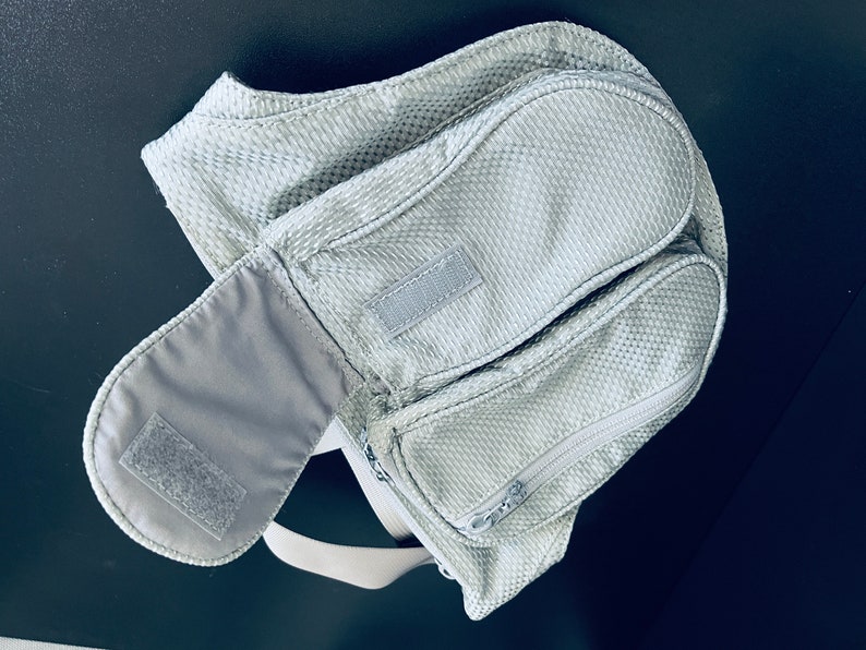 K&ouml;nnte beinhalten: Eine graue Mesh-Bauchtasche mit zwei Rei&szlig;verschlussf&auml;chern und einer Klettverschlusslasche. Die Tasche hat einen Trageriemen.