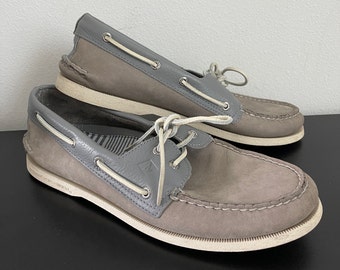 May include: A pair of gray leather boat shoes with white laces. The shoes have a white rubber sole and a gray leather upper. The shoes are in good condition and have a classic boat shoe style.