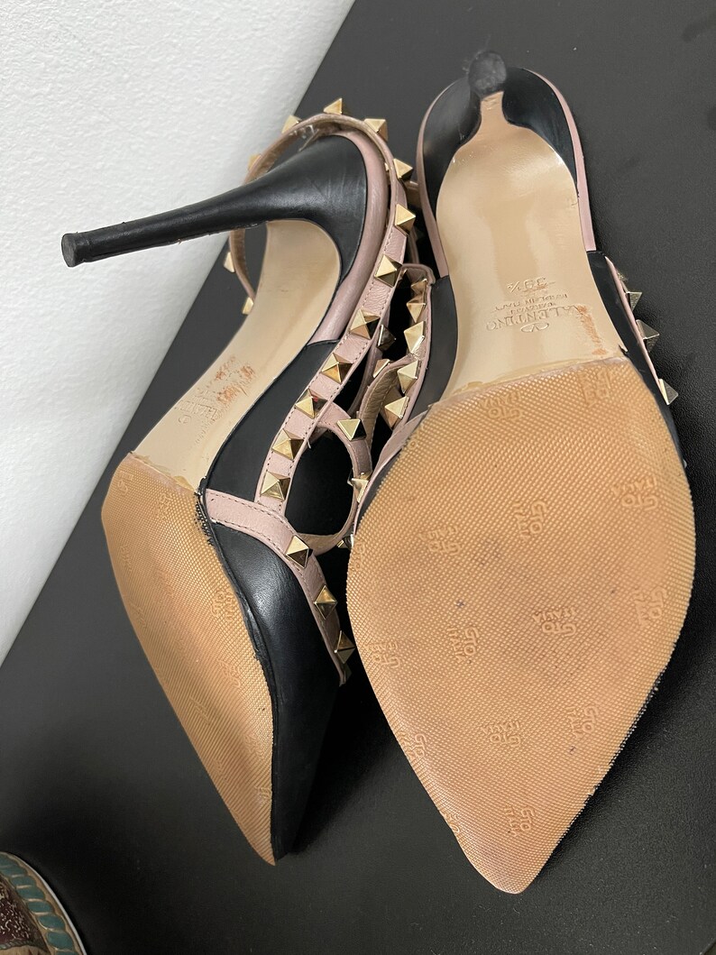May include: Black and pink leather high heel shoes with gold studs and a Valentino logo on the sole.
