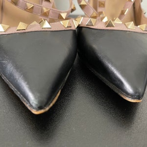 May include: A pair of black and nude leather heeled shoes with gold pyramid studs. The shoes have a pointed toe and a stiletto heel.