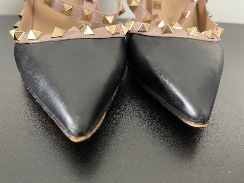 May include: A pair of black and nude leather heeled shoes with gold pyramid studs. The shoes have a pointed toe and a stiletto heel.