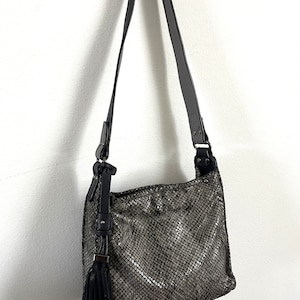 May include: A gray snakeskin-textured crossbody bag with a black tassel and adjustable strap.
