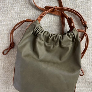 May include: A green canvas bucket bag with brown leather straps and a drawstring closure.