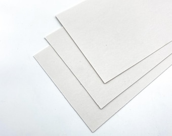 Könnte beinhalten: Drei Blätter weißes Kartonpapier, übereinander gestapelt.