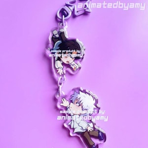 May include: A clear acrylic keychain featuring two connected charms of anime-style characters with white hair and dark hair, both wearing white shirts and dark pants. The text animatedbyamy is printed on the charms and the top metal star clasp.