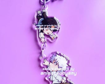 May include: A clear acrylic keychain featuring two connected charms of anime-style characters with white hair and dark hair, both wearing white shirts and dark trousers. The text animatedbyamy is printed on the charms and the top metal star clasp.