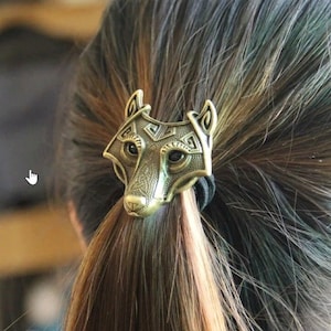 May include: A gold-toned wolf head hair tie with intricate details. The wolf's eyes are black and the hair tie is made of a black elastic band.