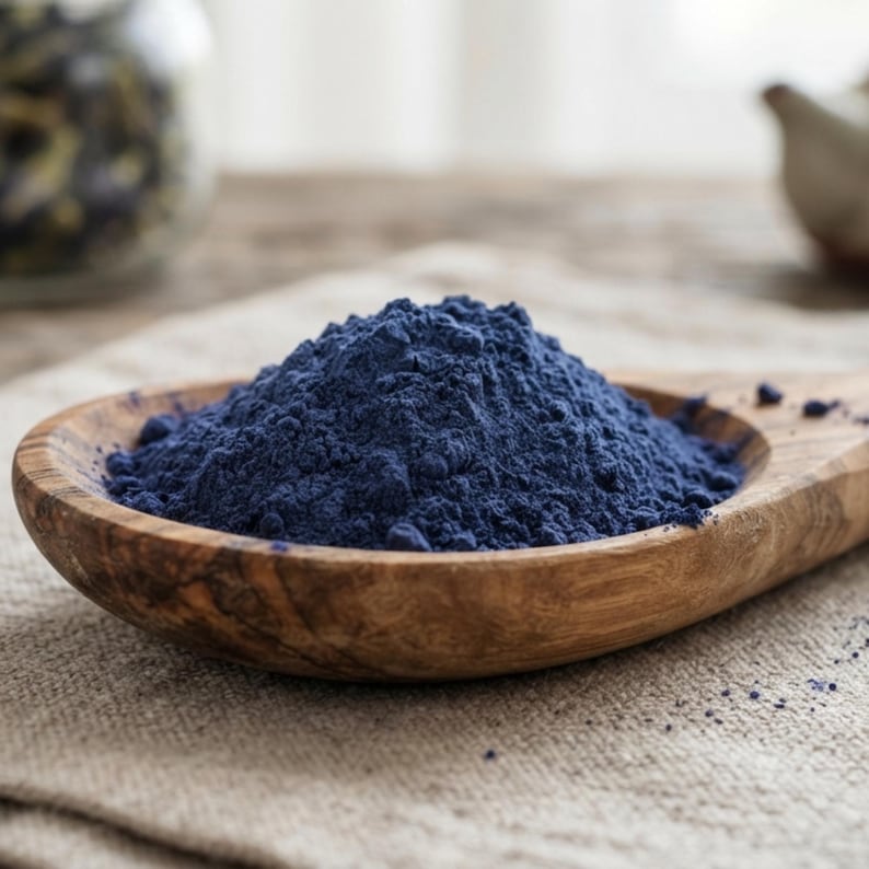 K&ouml;nnte beinhalten: Ein H&auml;ufchen feines, tiefblaues Pulver liegt mittig in einem flachen, ovalen Holzl&ouml;ffel mit sichtbarer nat&uuml;rlicher Maserung. Die Textur des Pulvers wirkt weich und gleichm&auml;&szlig;ig und bildet einen Kontrast zur glatten, polierten Oberfl&auml;che des Holzes.