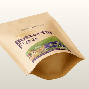 K&ouml;nnte beinhalten: Ein beigefarbener Standbeutel mit Schmetterlingsbl&uuml;tenpulver. Das Etikett zeigt den Text lotusfactory, Butterfly Pea und Flower Powder sowie eine grafische Darstellung von violetten Bl&uuml;ten, einer gelben Sonne und einer kleinen Gruppe von Menschen.