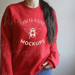 以下が含まれることがあります： 前面に白い蜂のグラフィックと「THREAD HOUSE MOCKUPS」の文字が印刷された赤いスウェットシャツです。