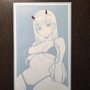 Puede incluir: Una pegatina rectangular con una ilustración de estilo anime en blanco de una mujer en bikini con cuernos rojos. El fondo es azul claro y la pegatina tiene un borde blanco. El texto "vinylpalm.com" está en la parte inferior.