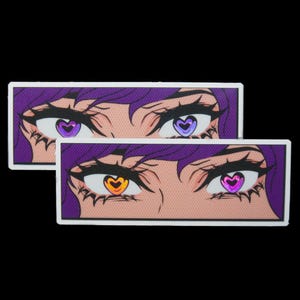 May include: Two rectangular stickers featuring anime-style eyes with purple hair. The eyes have heart-shaped pupils in purple, orange, and pink. The stickers have a white border and a black background.
