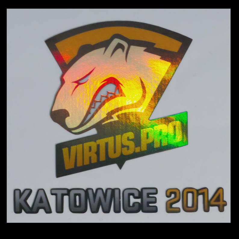 May include: A holographic sticker featuring the Virtus.pro logo, which depicts a stylized bear head in profile with sharp teeth, set against a shield-like background. Below the logo, the text KATOWICE 2014 is printed in bold, dark lettering.