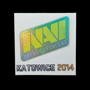 May include: A square white sticker featuring a holographic NaVi logo with the text Natus Vincere in a slanted rectangular frame. Below the logo, the text KATOWICE 2014 is printed in bold, dark gray capital letters on the white background surface.