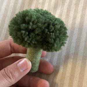 May include: A green pom-pom tree with a green felt trunk. The tree is about 4 inches tall.