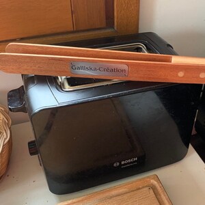 Peut inclure: Un grille-pain noir avec une étiquette argentée indiquant "Bosch" et une paire de pinces en bois avec une étiquette argentée indiquant "Galliska-Creation".