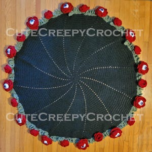 May include: A round, dark green crocheted blanket with a spiral design. The edge is decorated with red roses and green leaves, each rose featuring a blue and white eyeball. The text "Cute Creepy Crochet" is visible.