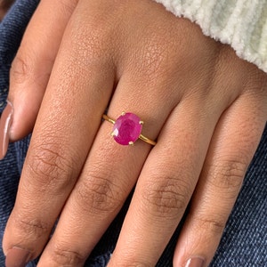 May include: A gold ring with a large, oval-shaped, pink gemstone set in a prong setting.