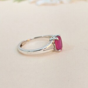 Puede incluir: Un anillo de plata con una piedra preciosa de corte ovalado en un tono rojo rosado vibrante, montada en un engaste de cuatro garras. La banda presenta un dise&ntilde;o de brazo dividido que se estrecha hacia la montura, con acabado pulido.