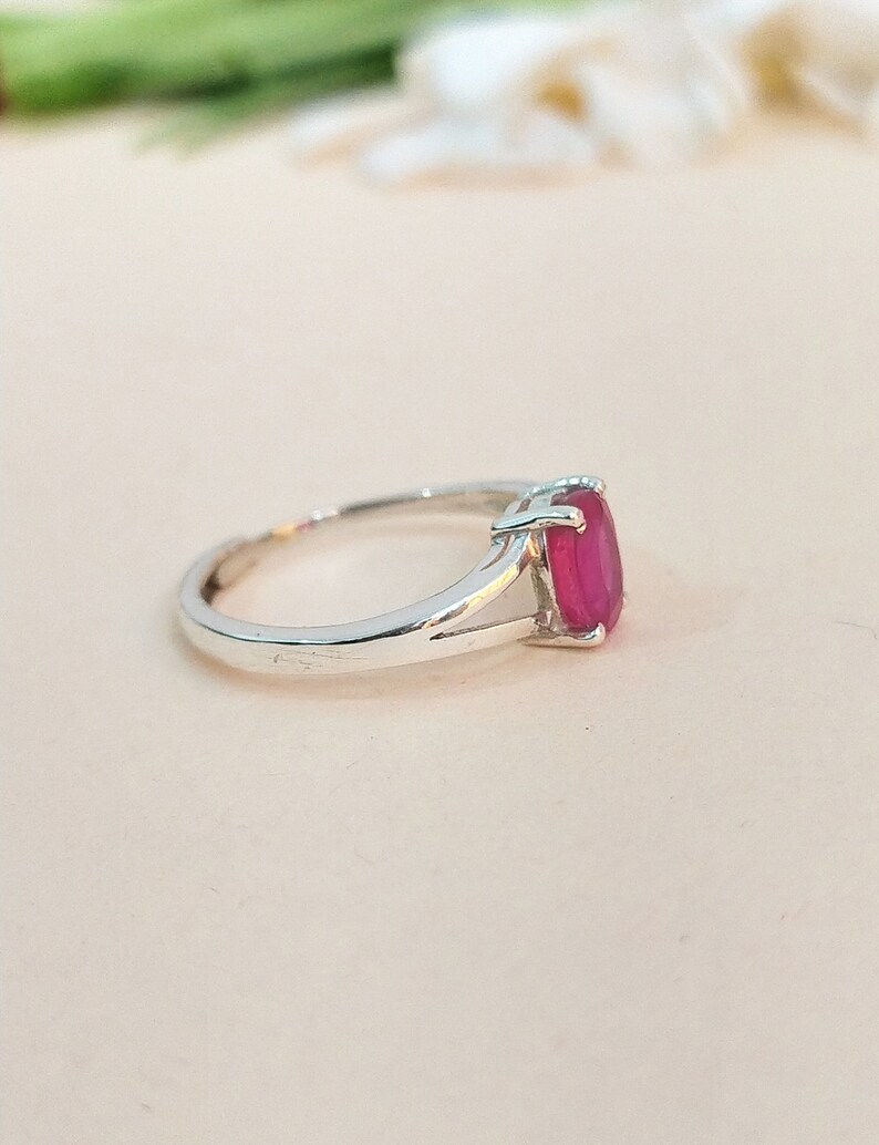 Puede incluir: Un anillo de plata con una piedra preciosa de corte ovalado en un tono rojo rosado vibrante, montada en un engaste de cuatro garras. La banda presenta un dise&ntilde;o de brazo dividido que se estrecha hacia la montura, con acabado pulido.