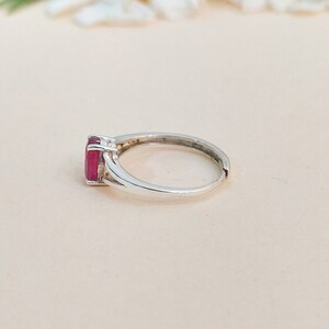 Puede incluir: Un anillo de plata con una piedra preciosa rectangular facetada de color rosa intenso, montada en un engaste de cuatro garras. La banda es lisa y met&aacute;lica, con un dise&ntilde;o de v&aacute;stago dividido cerca del engaste y una abertura visible atr&aacute;s.