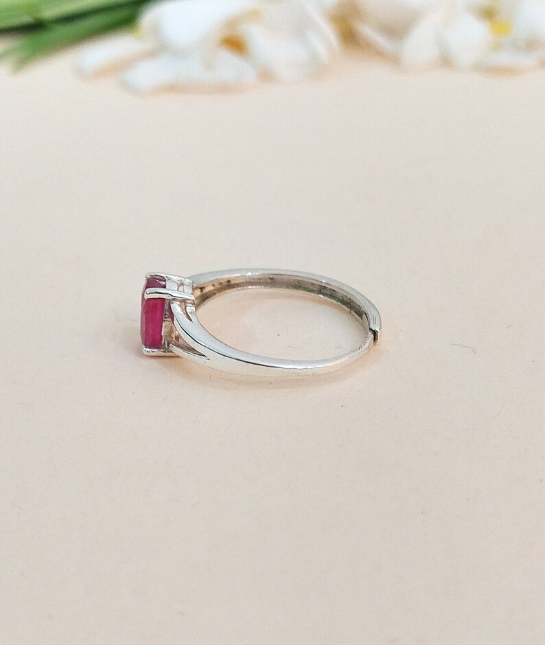 Puede incluir: Un anillo de plata con una piedra preciosa rectangular facetada de color rosa intenso, montada en un engaste de cuatro garras. La banda es lisa y met&aacute;lica, con un dise&ntilde;o de v&aacute;stago dividido cerca del engaste y una abertura visible atr&aacute;s.