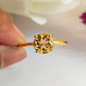 Puede incluir: Un anillo de oro con una piedra preciosa redonda, transparente y amarilla engastada en un engaste de cuatro garras.